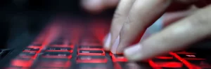 header hacker typing on red lit laptop keyboard
